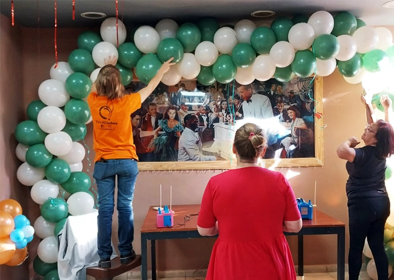 Alumnos colgando un arco de globos blancos y verdes opaco en la pared.