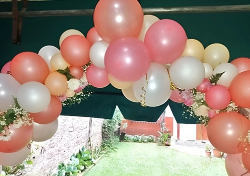 Arco de globos blancos y rosados con decoración de flores.