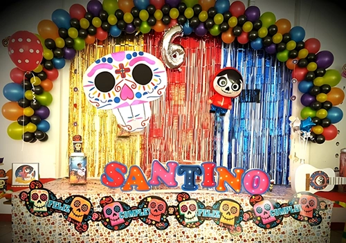 Decoración de cumpleaños, temática película Coco. Se ve un arco de globos, globo del personaje Coco y el número seis.