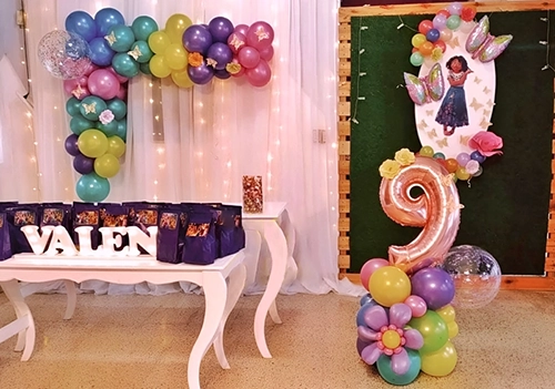 Decoración de cumpleaños, temática película Encanto. Se ve un arco ele de globos, una columna y flor de globos, el número nueve y mariposas
