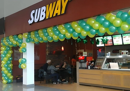 Arco de globos amarillos y verdes, decorando la entrada del local Subway