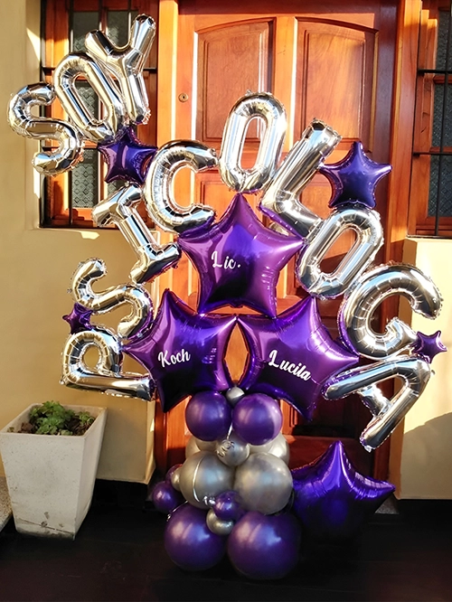 Bouquet de globos letras plateadas formando la palabra Soy Psicóloga, unidas con globos estrella violeta, sobre base de globos opacos viletas y plateados.